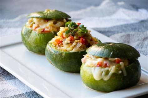 Fotografía de zapallitos italianos rellenos recién horneados, decorados con hierbas frescas y acompañados de arvejas coloridas