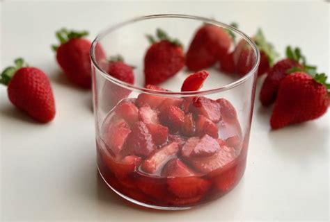 Fotografía profesional de una copa de cristal rellena con capas de fresas maceradas y crema chantilly, decorada con anises de colores y una hoja de romero.