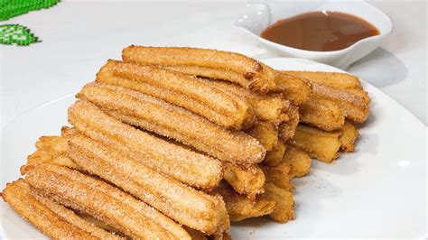 Imagen de unos churros recién hechos, dorados y espolvoreados con azúcar y canela, con el relleno de dulce de leche asomándose por los extremos.