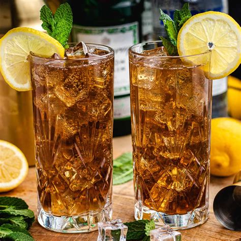 Ingredientes básicos para Long Island Iced Tea: botellas de vodka, ron, ginebra, tequila, triple seco, zumo de limón, jarabe de azúcar y cola, junto a un vaso lleno de hielo.
