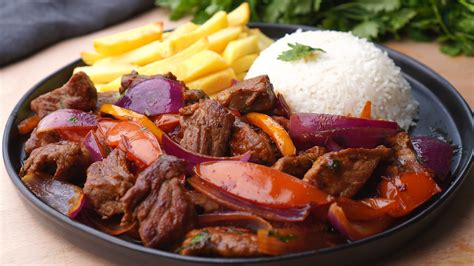 Fotografía profesional de un lomo saltado servido en un plato grande, mostrando la carne jugosa, verduras brillantes y las papas fritas mezcladas con el arroz blanco al costado.