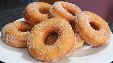 Primer plano de donas caseras recién fritas y escurriéndose sobre papel absorbente.
