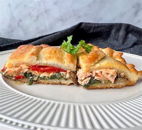 Empanada de salmón y espinacas sobre tabla de madera, con una porción cortada mostrando el relleno