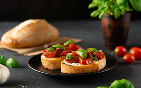 Primer plano de los ingredientes frescos para bruschetta: tomates, albahaca, ajo, pan y aceite de oliva.