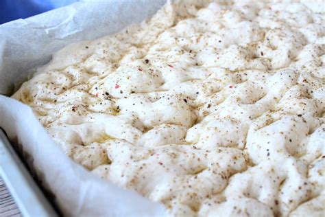 Foto detallada de una focaccia antes de hornear, con los agujeros característicos y toppings ya colocados