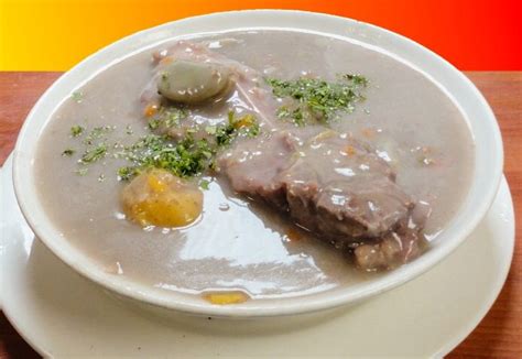 Sopa de cuchuco con espinazo de cerdo humeante en un plato, con aguacate y ají al lado