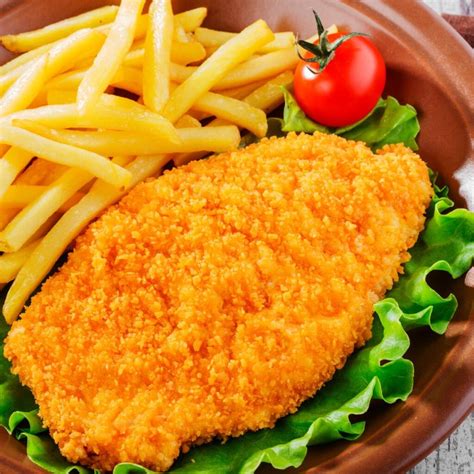 Fotografía gastronómica de pechugas de pollo empanizadas servidas con guarniciones clásicas.