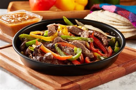 Plato de fajitas de frijoles con pimientos y cebolla, servidas con tortillas de maíz y aguacate.
