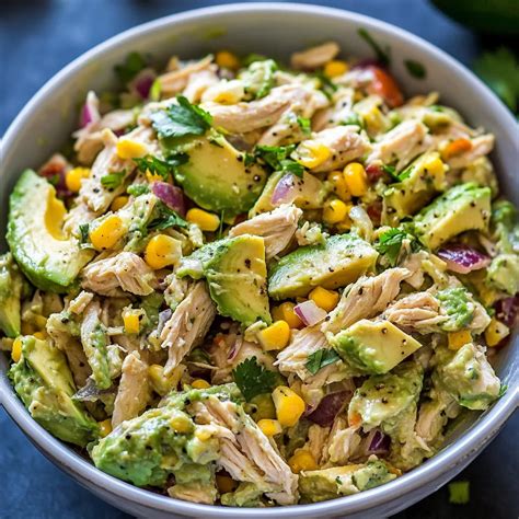 Ingredientes frescos para una ensalada de pollo y aguacate: pollo cocido, aguacate en cubos, limón y hierbas.