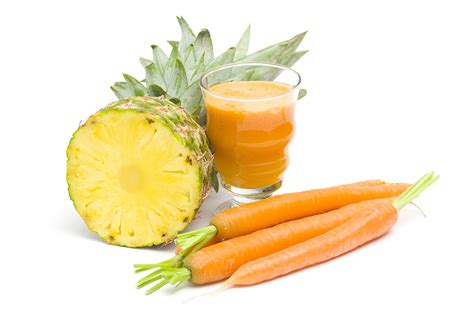 Jugo cremoso de zanahoria y piña en un vaso, con ingredientes frescos al lado