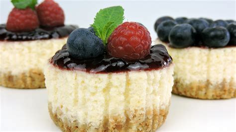 Una selección de mini tartas de queso (cheesecakes) decoradas con frutas del bosque, presentadas en un plato elegante.