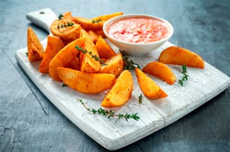 Fotografía de papas rústicas cortadas en gajos, doradas y condimentadas con hierbas frescas.