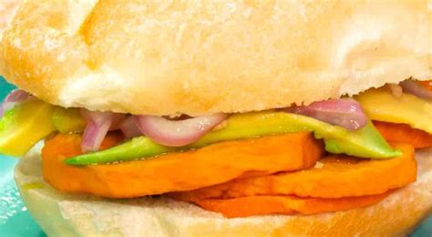 Pan con chicharrón peruano servido con camote frito y sarsa criolla en un pan francés