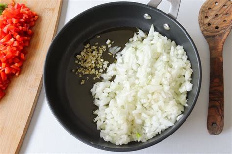 Un chef preparando un sofrito de cebolla, ajo y pimiento en una sartén grande.