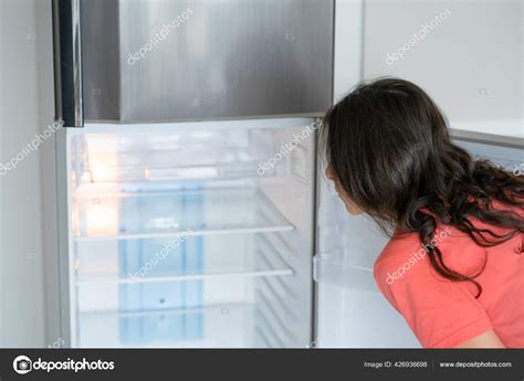Persona mirando un refrigerador vacío en busca de ingredientes para cocinar