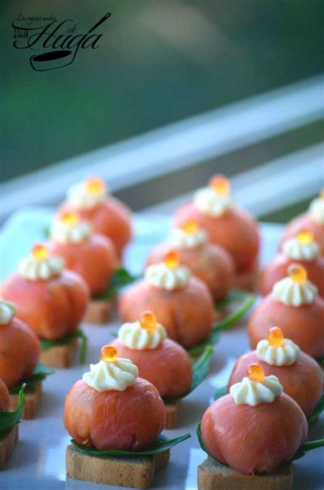 Plato de presentación con bombones de salmón decorados con frutos secos sobre cucharillas de aperitivo