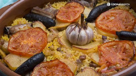 Arroz al horno valenciano presentado en una cazuela de barro, decorado con patatas, tomate, morcilla y una cabeza de ajos en el centro.