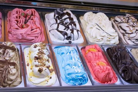 Imagen de diversas variedades de helados artesanales servidos en copas y conos, decorados con frutas frescas y frutos secos.