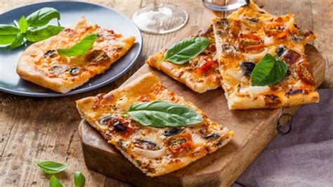 Fotografía de una pizza siciliana rectangular con una base gruesa y cubierta con ingredientes tradicionales.