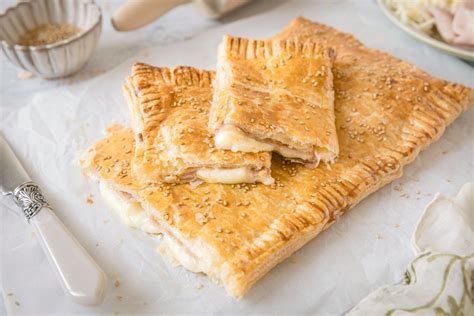 Imagen de una empanada de hojaldre de jamón y queso recién horneada, dorada y crujiente sobre una bandeja de cocina.
