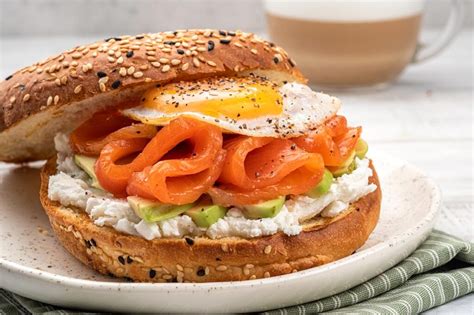 Bagel abierto mostrando capas de queso crema, salmón ahumado, cebolla morada y lechuga.