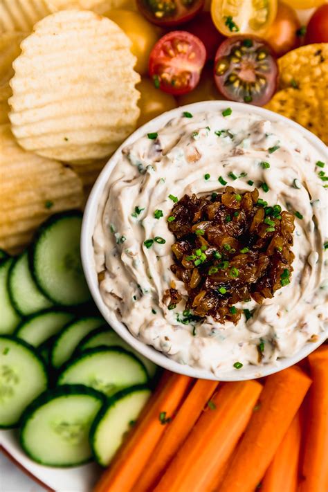 Bowl de dip de ranch cremoso con trozos de cebolla caramelizada, acompañado de bastones de vegetales.
