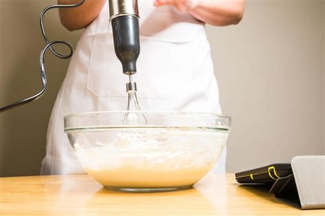 Primer plano de una persona mezclando una crema en un bowl sobre un baño María