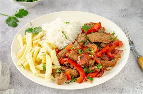 Plato de lomo saltado con carne y verduras servido con arroz y papas fritas