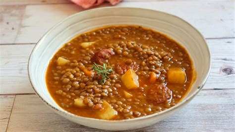 Plato de lentejas humeantes con trozos de chuleta ahumada y chorizo, acompañadas de arroz blanco.