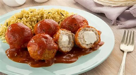 Fotografía de albóndigas rellenas de queso y tocino, plato final servido con salsa y perejil.