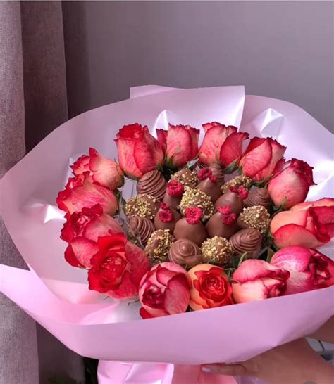 Fotografía de un ramo artesanal que combina rosas frescas con frutillas bañadas en chocolate decoradas con hilos dorados y blancos.