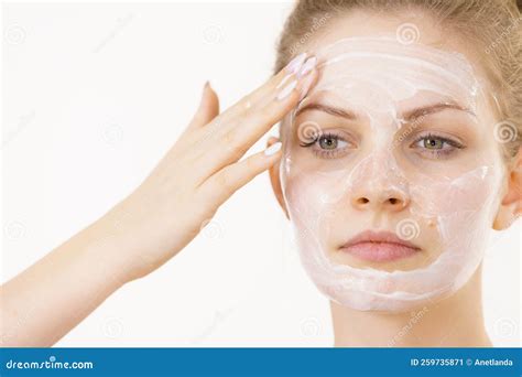 Thematic photo of a woman applying a facial mask with goat milk, or a cosmetic product with goat milk on elegant packaging.