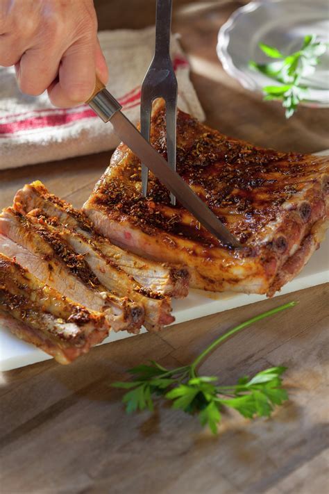 Costillar de cerdo asado y cortado, servido con acompañamientos y una copa de vino tinto
