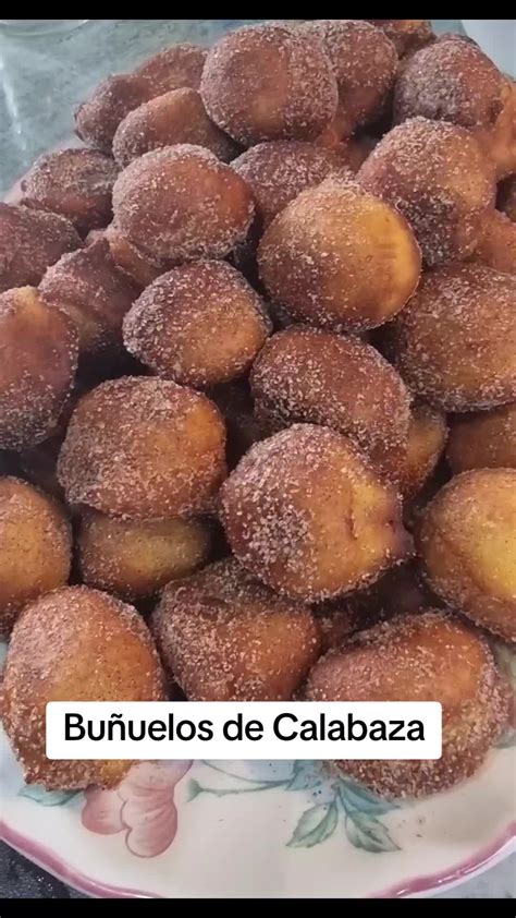 Buñuelos escurriéndose en un colador y siendo rebozados en azúcar