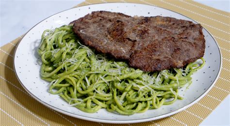 Plato servido de tallarines verdes cubiertos con un bistec de ternera recién hecho