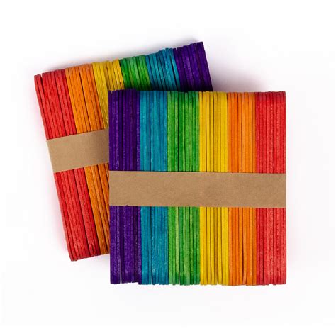Imagen que muestra una variedad de palos de helado de colores, pegamento y accesorios de manualidades sobre una mesa de trabajo.