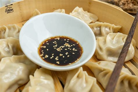 Mesa de cocina con ingredientes frescos para gyozas: cebolletas, jengibre, col, carne picada, especias.