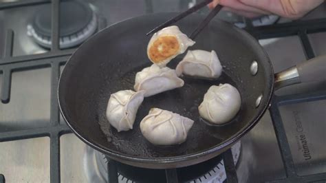 Gyozas dorándose en una sartén, con vapor saliendo de debajo de la tapa.