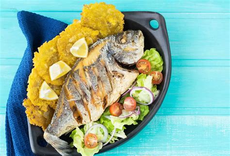 Mesa con todos los ingredientes frescos para pescado frito y arroz con vegetales, incluyendo cebolla, ajo, zanahorias, choclo, arverjas, vainitas, pimiento, arroz y filetes de pescado.