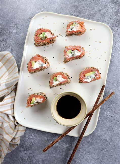 Fotografía de un plato de sushi ligero sin arroz con salmón, mostrando los rollitos cortados y decorados con semillas de sésamo y salsa de soja.