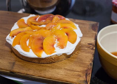 Fotografía de una torta de duraznos terminada, con capas visibles de bizcocho, crema y duraznos, decorada elegantemente.