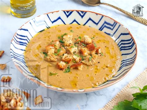 Fotografía de un plato hondo con crema de lentejas decorada con carne molida dorada y hierbas frescas.