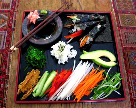 Mesa de ingredientes frescos para preparar sushi: arroz, algas nori, aguacate, salmón, surimi, queso crema, zanahoria, pepino y pan molido