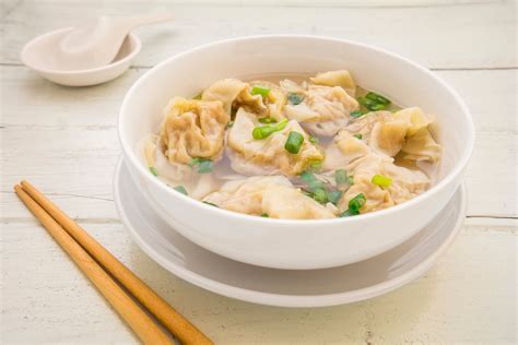 Cuenco de sopa wonton con dumplings flotando y cebolleta fresca.