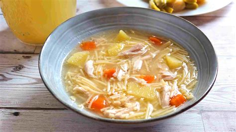 Imagen de una sopa de pollo humeante servida en un plato hondo con verduras troceadas y pasta.