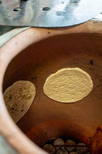 Horno tandoor tradicional con pan naan cocinándose en su interior