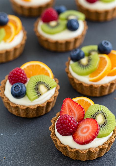 Tartaletas de frutas coloridas y variadas, decoradas con hojas de menta y un ligero brillo.