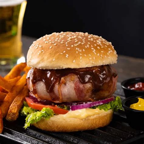 Foto de una hamburguesa rellena de queso envuelta en tocino, cocinada y lista para servir