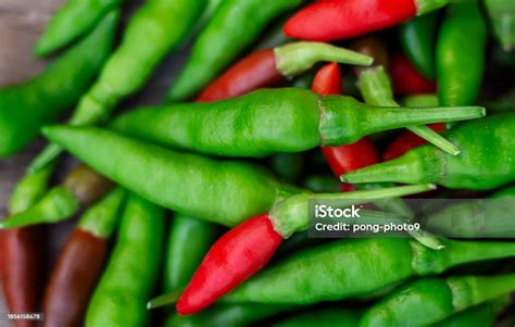 Foto macro de chiles ojo de pájaro rojos frescos sobre un fondo oscuro, con algunas hojas verdes