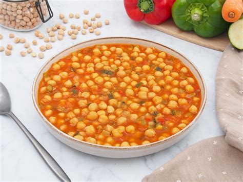 Fotografía cenital de un plato de barro con garbanzos guisados humeantes, destacando su textura cremosa y un fondo rústico con especias.